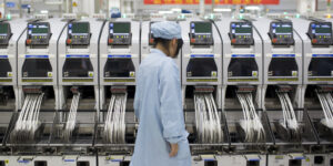 An employee monitors machinery used to adhere components to smartphone circuit boards in a manufacturing facility at ZTE Corp.'s headquarters in the Nanshan district of Shenzhen, China, on Thursday, Aug. 7, 2014. ZTE, a Chinese maker of telecommunications equipment and systems, is scheduled to report second quarter earnings on Aug. 20. Photographer: Brent Lewin/Bloomberg via Getty Images